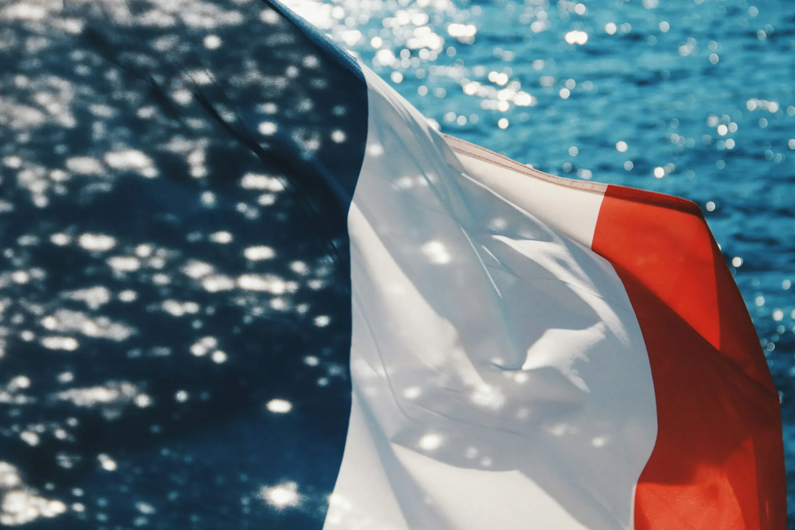 Drapeau français flottant au vent sur fond de mer scintillante.