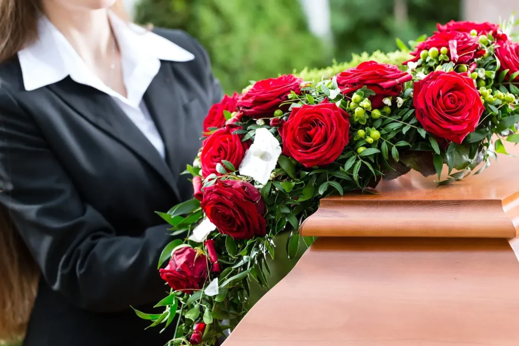 Composition de roses rouges posée délicatement sur un cercueil en bois.